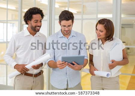 Three young business colleagues using digital tablet with blueprints in the office