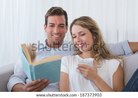 Relaxed young couple reading book on couch at home
