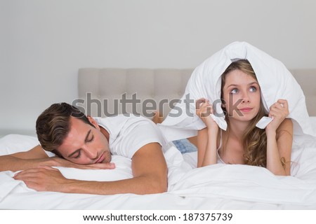 Angry young woman holding pillow besides a sleeping man in bed at home