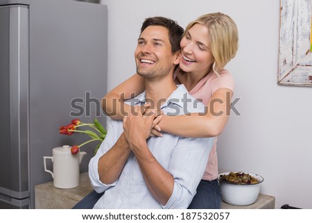 Portrait of a cheerful young woman embracing man from behind in kitchen at home