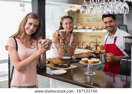 Smiling woman drinking coffee with friend and male barista at counter in the coffee shop