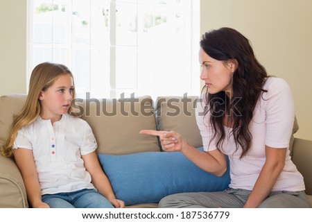 Young mother scolding girl while sitting on sofa at home