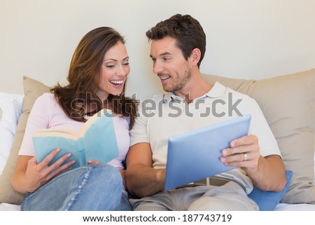 Relaxed happy young couple with laptop and book sitting on couch at home