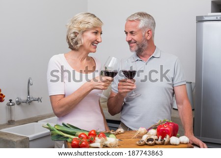 Happy mature couple toasting wine glasses while preparing food in the kitchen at home