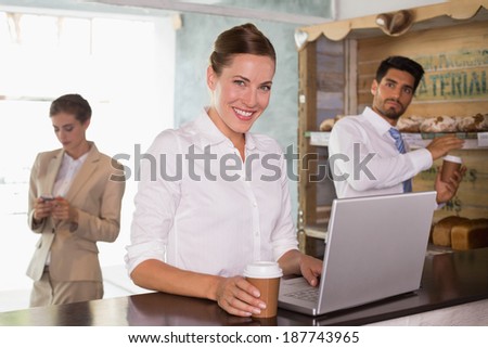 Businesswoman using laptop with colleagues behind in office cafeteria