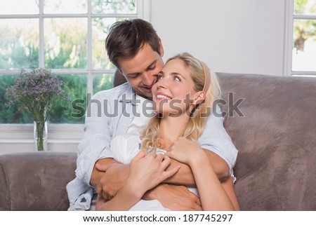 Relaxed happy loving young man embracing woman from behind in living room at home