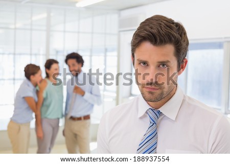 Colleagues gossiping with sad young businessman in foreground at a bright office