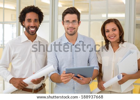 Portrait of three young business colleagues with blueprints and digital tablet in the office
