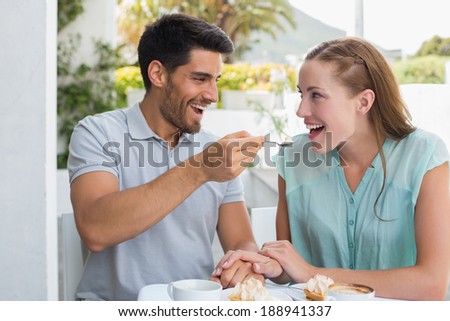 Portrait of a happy young man feeding woman at the coffee shop