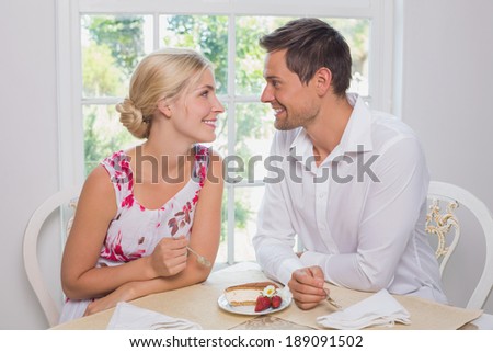 Happy loving young couple with pastry looking at each other at dining table at home
