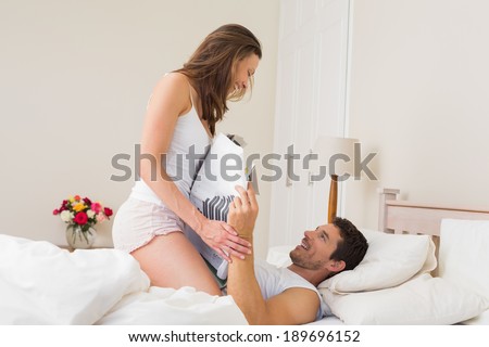 Side view of a young woman sitting on man as he reads newspaper in bed at home