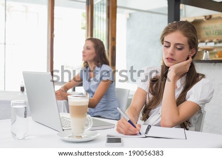 Concentrated young woman writing notes with laptop in the coffee shop