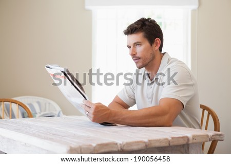 Side view of a concentrated young man reading newspaper at table