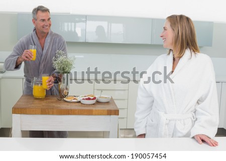 Portrait of a smiling woman and man with orange juice in background in the kitchen at home