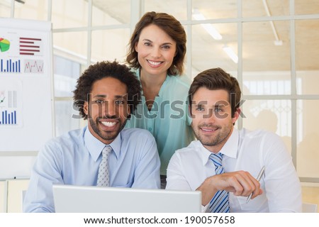 Portrait of three smiling young business people using laptop together at office