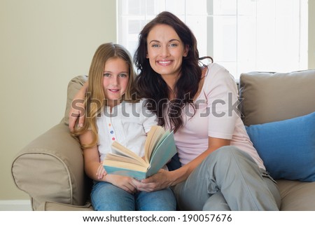 Portrait of mother and daughter holding book while sitting on sofa at home