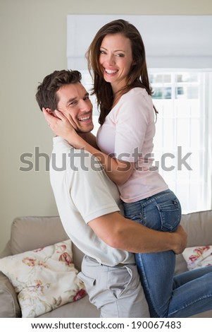 Side view portrait of a happy young man carrying woman at home