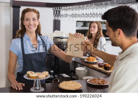 Friendly female cafe owner giving packed food to a couple at the coffee shop