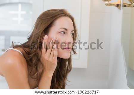 Side view of a beautiful young woman examining her face in the bathroom at home