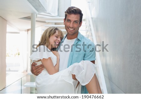 Portrait of a smiling young man carrying woman against stairs at home