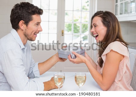 Side view of a young man giving happy woman a gift box at home
