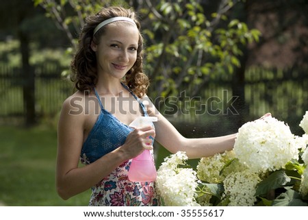 Beautiful girl is using sprinkler for watering flowers. Focus on face.
