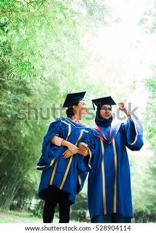 Portrait of happy young female graduates in academic dress and square academic cap hugging. Selective focus. Toned image.