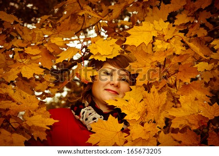 Smiling young woman face among the maple leaves. With dark vignette effect