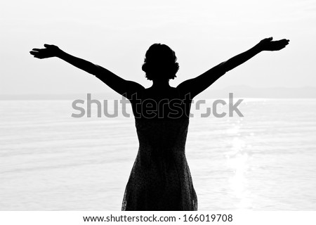Meeting a sun. Silhouette of young beautiful woman at seashore.  Black and white photo