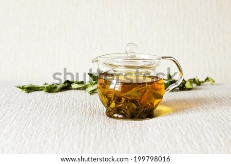 Green tea in glass teapot with fresh dry mint leaves on textured linen background. Focus on teapot