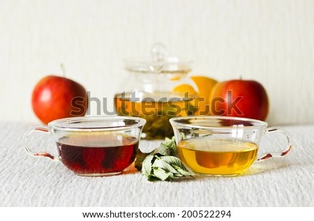 Still life: green tea in glass teapot, green and strong black tea in glass cups, mint leaves, fruits: apples, orange. Selective focus on cups