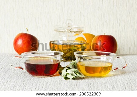 Still life: green tea in glass teapot, green and strong black tea in glass cups, mint leaves, fruits: apples, orange