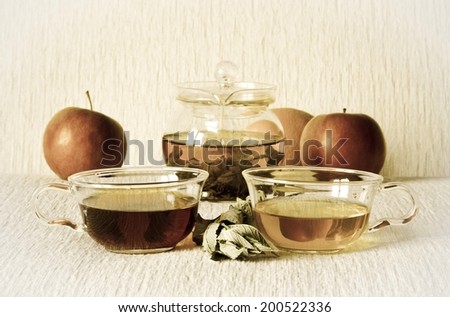 Vintage still life: green tea in glass teapot, green and strong black tea in glass cups, mint leaves, fruits: apples, orange