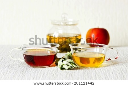 Still life: green tea in glass teapot, green and strong black tea in glass cups, mint leaves, fruits: apple