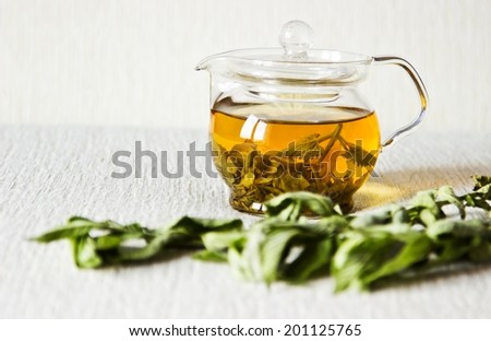 Green tea in glass teapot with fresh dry mint leaves on textured linen background. Focus on teapot