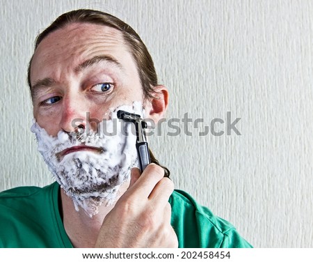 Closeup of handsome young man shaving face with razor blade