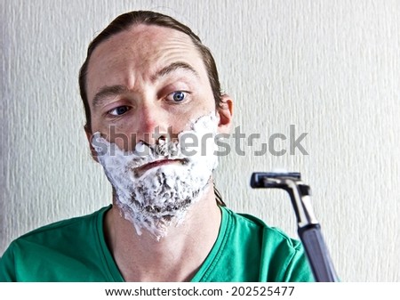 Portrait of handsome bearded young man with foam on face afraid to shaving