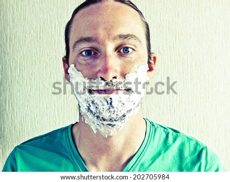 Portrait of handsome bearded young man with shaving foam on face. Image with vintage filter