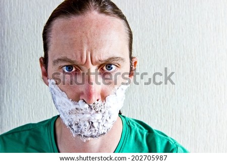 Portrait of handsome bearded young angry man with shaving foam on face