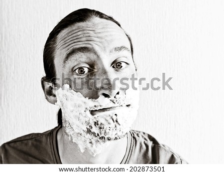 Portrait of handsome bearded young man with shaving foam on funny face. Image toned in black and white colors