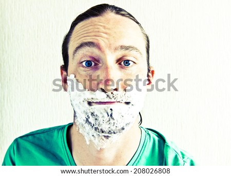 Portrait of handsome bearded young man with shaving foam on funny face. Image with vintage filter