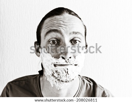 Portrait of handsome bearded young man with shaving foam on funny face. Image toned in black and white colors