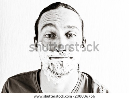 Portrait of bearded young man with shaving foam on funny face. Image toned in black and white colors