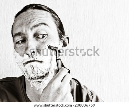 Closeup of handsome young man shaving face with razor blade. Black and white image
