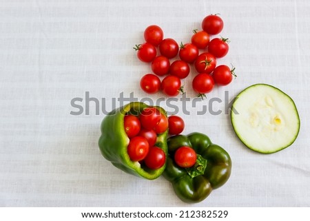 Small tomatoes in cut green pepper with zucchini slice at white linen background. Horizontal image. Objects at the right part of image