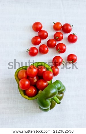 Small tomatoes in cut green pepper at white linen background. Vertical image