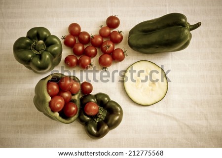 Small tomatoes in cut green pepper with zucchini slice at white linen background. Horizontal image with vintage filter