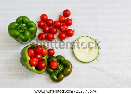 Small tomatoes in cut green pepper with zucchini slice at white linen background. Horizontal image