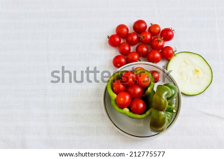Small tomatoes in cut green pepper with zucchini slice at white linen background. Horizontal image. Objects at the right part of image