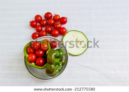 Small tomatoes in cut green pepper with zucchini slice at white linen background. Horizontal image. Objects at the left part of image